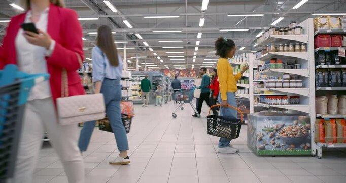 Variety of Young Customers Browsing Shop Aisles of a Stocked Grocery Store. Men and Women Pick Out Vegetables, Check Expiry Dates and Load Their Carts With Weekly Essentials