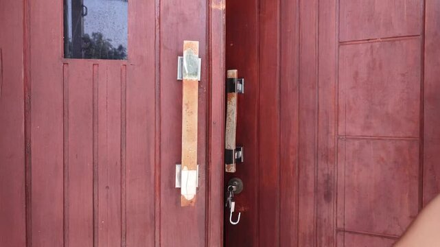 Opening a brown wooden door with a key and padlock hanging on the door