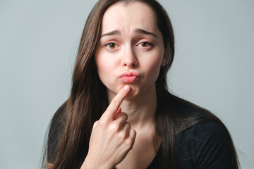 Naklejka premium Virus herpes on lips close-up. Unhappy woman shows on a painful swollen lips. Portrait of young beautiful girl of European appearance with infection injury. Dermatology sickness. Facing treatment