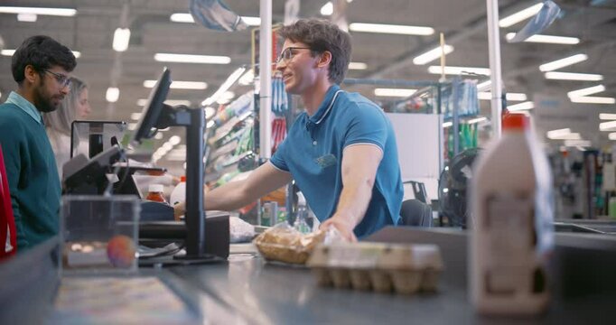Young Cashier Working at a Supermarket Checkout. Worker Scanning Groceries for Customers at a Store Counter. Customers Waiting Patiently as the Cashier Processes the Items and Prepares the Bill
