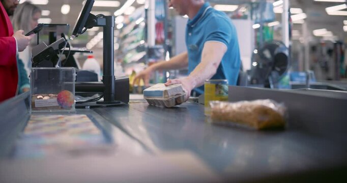 Young Male Cashier Working Behind the Register, Scanning Items at the Supermarket Checkout. His Concentration Ensures that Each Product Is Correctly Entered Into the System