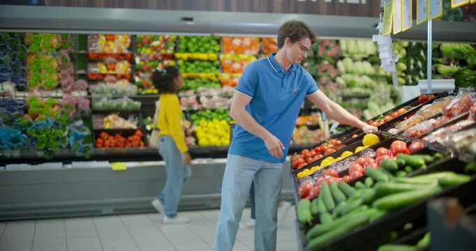 Handsome Male Worker Bringing a Box Case of Tomatoes to a Supermarket Vegetable Aisle, Making Sure Each Product is Fresh. Portrait of a Young Worker in Glasses Looking at Camera and Smiling
