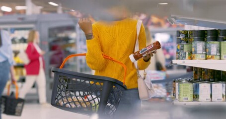 Cinematic Footage of an African Woman Standing in a Grocery Aisle, Carefully Examining the Labels and Selecting Food Items From the Shelf. Adding Peas and Ketchup to Her Shopping Cart