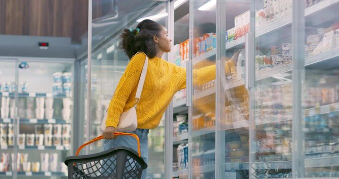 Young Black Woman Standing in Front of the Refrigerated Section, Opening the Fridge to Grab a Bottle of Milk. She Quickly Adds Them to Her Basket, Planning Her Next Grocery Choices