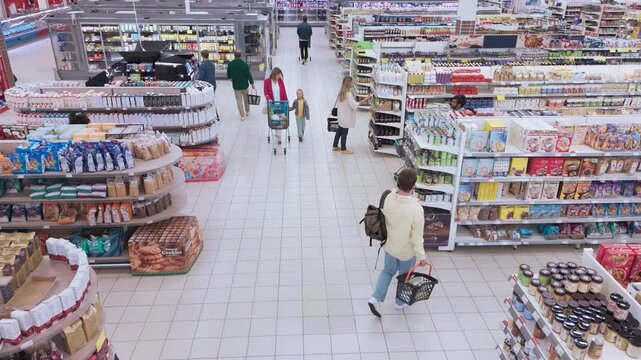 Aerial Footage of a Group of Diverse Consumers, Including Children and Adults, Moves Through a Supermarket. Families Pick Out Groceries and Dairy Products, while Some Check Offers on Packaged Foods