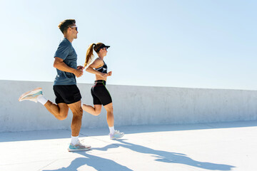 Two Young Adults Jogging on a Rooftop Under Bright Blue Skies During a Sunny Day, Showcasing Fitness and Outdoor Activity