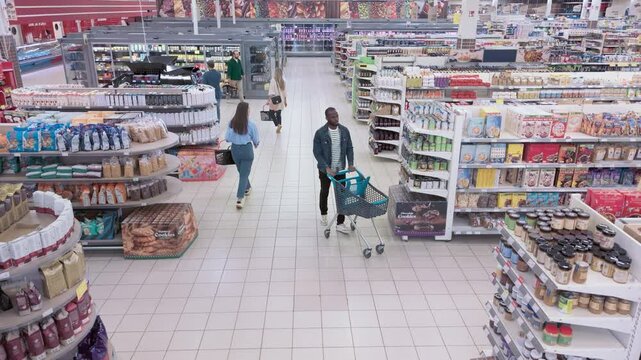 Group of Diverse Shoppers, Including Children and Adults, Move Through a Supermarket. Customers Carrying Fresh Fruits and Vegetables in a Cart Together with Some Packaged Foods. Aerial Footage