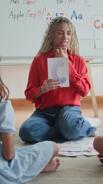 Vertical shot of female Hispanic speech therapist and two kids having interactive lesson when sitting on floor in classroom