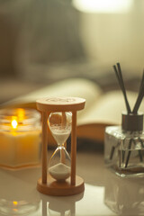 Time to relax - an hourglass in a cozy setting with an open book, a candle and fragrance sticks on...