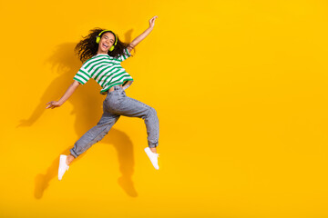 Full body portrait of nice young girl jump run headphones empty space wear striped t-shirt isolated on yellow color background