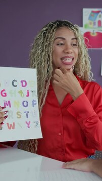 Vertical shot of young female Hispanic logopedist demonstrating correct pronunciation of letters at session