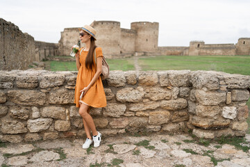 Fototapeta premium Tourist in ancient fortress drinks cocktail near castle at sunset