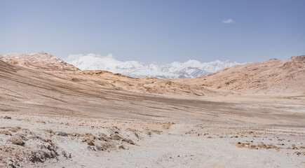 Dusty road of the Pamir Highway winds and twists in the valley of the Tien Shan mountains in Tajikistan in Pamir, landscape in the high desert mountains for background