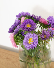 A vibrant bouquet of purple and pink aster flowers in a clear glass vase, ideal for Mother's Day