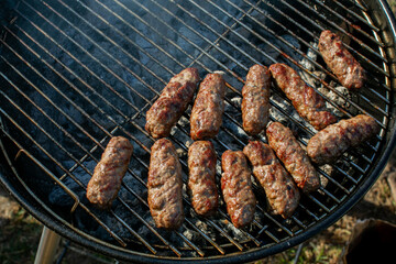 Grilling traditional homemade Romanian mici sausages on a charcoal barbecue grill during a summer backyard cookout