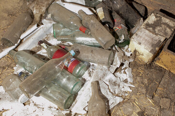 Abandoned dirty wine bottles pile in a cluttered basement, highlighting waste management and...