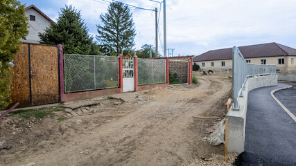 Rural dirt road leading to residential houses, illustrating infrastructure challenges and urban development in small European village settings