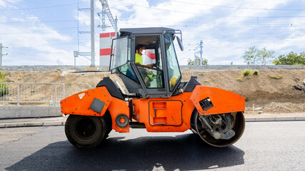 A worker operates an industrial steamroller on a sunny day, symbolizing construction and infrastructure development
