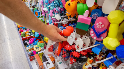 A person's hand selecting colorful dog toys from a diverse display in a pet store, highlighting pet...