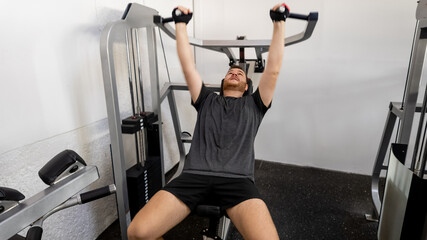 Fototapeta premium A Caucasian man exercises on a chest press machine in a gym, emphasizing fitness and health during New Year's resolutions