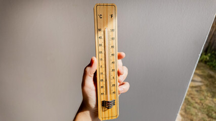 A hand holding a wooden thermometer indicates rising temperatures, highlighting concerns about global warming and climate change effects