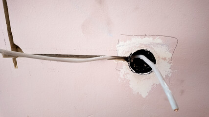 Electric wiring installation in progress with exposed cables through wall socket, relevant to home renovation and electrical safety concerns