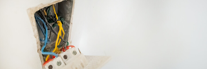 Close-up of exposed electrical wiring in a wall socket, highlighting the risk of electrical hazards and DIY repair challenges