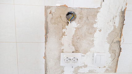 Damaged wall with exposed electrical wiring and socket during home renovation, highlighting safety concerns in electrical maintenance