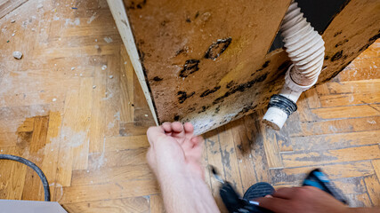 A person examines mold growth and water damage under a kitchen sink, highlighting household...