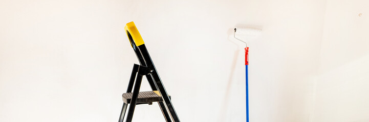 A stepladder and a paint roller against a white wall, concept: home renovation and DIY projects