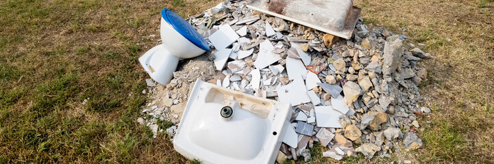 Broken bathroom fixtures and debris scattered on lawn illustrating renovation or remodeling waste...
