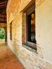 Obraz premium A peaceful Buddha statue is partially visible through a window in an old brick temple, with warm sunlight illuminating the rustic corridor outside.