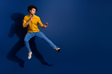 Fototapeta premium Full body portrait of nice young man jump fight empty space wear yellow shirt isolated on dark blue color background