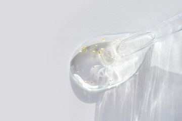 Transparent serum with dropper and gold flakes on white background - minimalist beauty and skincare concept.