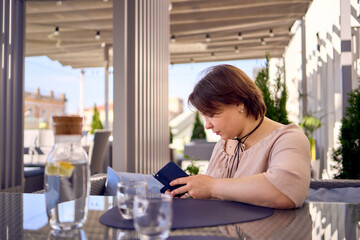 plus size woman in peach fuzz dress chooses a dish in a restaurant via QR code in smartphone, water...
