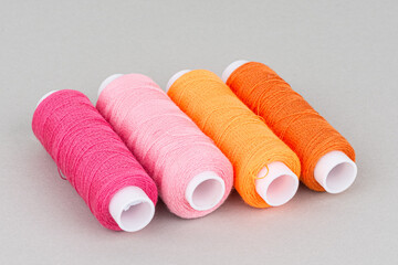 Red orange pink thread spools on grey background.