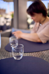 plus size woman in peach fuzz dress chooses a dish in a restaurant via QR code in smartphone, water with lemon and glasses in front of her