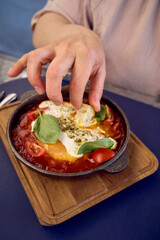 medium sized woman in peach fuzz dress eating Shakshouka in modern restaurant