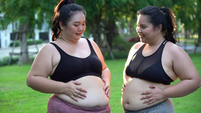Group of 2 overweight asian woman holding and show belly before exercise in Garden outdoors . two fat female friend warm up for workout outside . Body shaming
