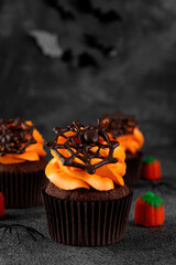 Halloween chocolate cupcakes with orange frosting and chocolate spider web on a dark background. Festive dessert. Funny food idea. Copy space.