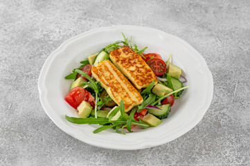 Salad with grilled halloumi cheese, tomatoes, avocado, cucumber and olive oil on a concrete background. Healthy food. Top view