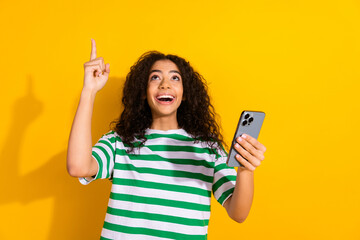 Portrait of nice young girl smart phone point finger up empty space wear striped t-shirt isolated...