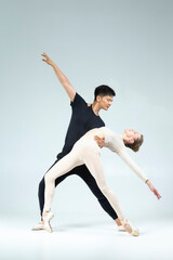 Modern Ballet Ideas. Professional International Sportive Couple of Asian Man and Caucasian Woman Performing As Ballet Dancers On Grey in Studio During Suppots © danmorgan12