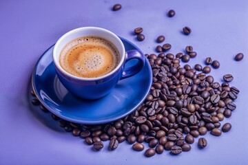 Fototapeta premium Aromatic Espresso in Vibrant Blue Cup Surrounded by Roasted Coffee Beans on Purple Surface