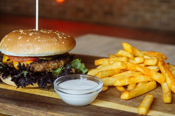 a hamburger with a toothpick stands on a cutting board with fries and a side dish