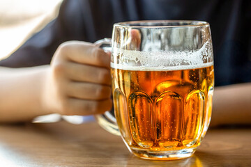 Man hand holding glass with beer in a bar or pub, bartender. Closeup of a man holding glass of beer. Hand of a male with full glass of beer at the pub. Close up of a woman hand holding glass beer