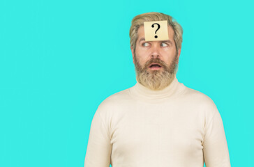 Surprised bearded man with question mark on blue background. Man with question mark on forehead looking up. Paper notes with question marks. Copy spase