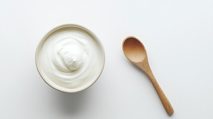 A bowl of yogurt on a white background with a wooden spoon next to it