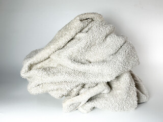 close up view of A worn-out, off-white towel is loosely folded with visible signs of aging and dirt, placed against a plain white background.
