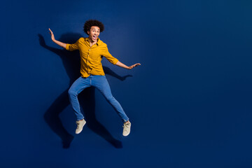 Obraz premium Full body portrait of nice young man jump empty space wear yellow shirt isolated on dark blue color background